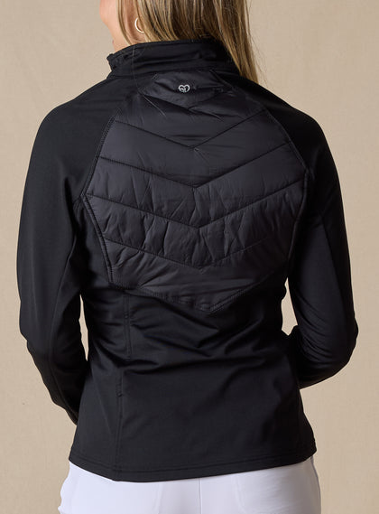 Nova Jacket in Black, back view on model featuring a black hybrid jacket with diagonal quilted upper back panel, stretch knit lower back and sleeves, and tonal logo detail at the center back neck styled with white pants