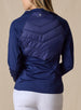 Nova Jacket in Indigo, back view on model featuring a navy hybrid jacket with diagonal quilted upper back panel, stretch knit lower back and sleeves, and tonal logo detail at the center back neck styled with white pants