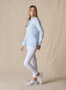 Women's Misty Top in Lake, full length side view on model featuring a solid light blue waffle knit long sleeve top with cowl neck and drawstring tie, paired with white pants and white shoes