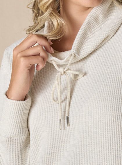 Women's Misty Top in Oatmeal, detailed close-up view on model featuring a cream waffle knit long sleeve top with cowl neck and drawstring tie