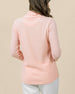 The back view of a woman modeling a soft peach waffle-knit cowl-neck long-sleeve top and white pants, set against a plain beige background.