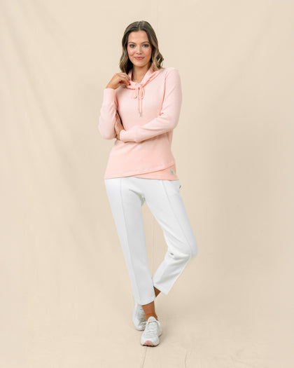 A woman modeling a soft peach long-sleeve pullover and white cropped pants against a neutral beige studio backdrop.