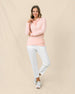 A woman modeling a soft peach long-sleeve pullover and white cropped pants against a neutral beige studio backdrop.