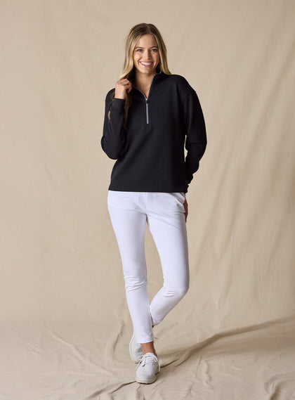 Women's Opal Half Zip in Black, full front view on model featuring a black waffle-textured pullover with a quarter-zip neckline paired with white pants and white golf shoes
