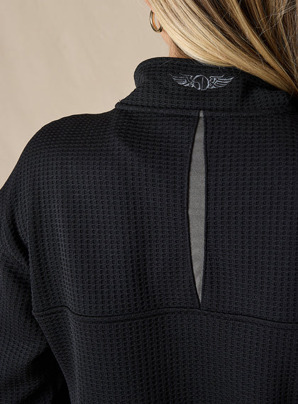 Women's Opal Half Zip in Black, close-up back detail view featuring the waffle-texture fabric, charcoal center back vent, and embroidered logo at the collar