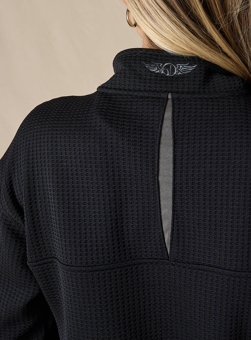 Women's Opal Half Zip in Black, close-up back detail view featuring the waffle-texture fabric, charcoal center back vent, and embroidered logo at the collar