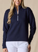 Women's Opal Half Zip in Indigo, front view on model featuring a navy waffle-textured pullover with a quarter-zip neckline and contrast white zipper paired with white pants