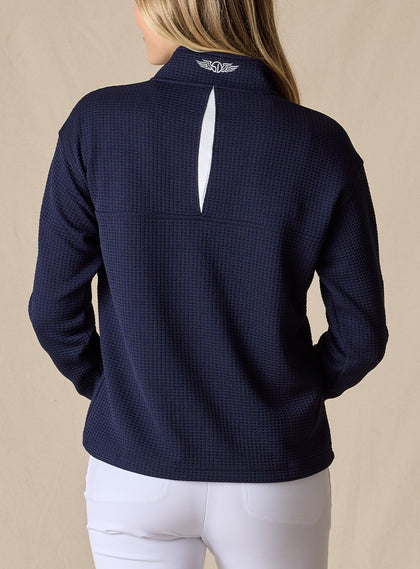 Women's Opal Half Zip in Indigo, back view on model featuring a navy waffle-textured pullover with an embroidered Straight Down logo at the collar and a white center back vent detail paired with white pants