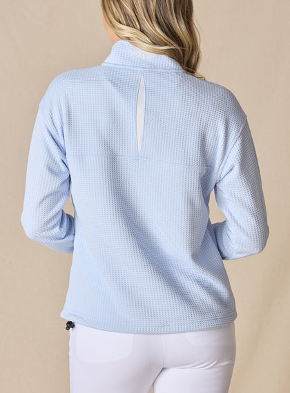 Women's Opal Half Zip in Powder, back view on model featuring a light blue waffle-textured pullover with an embroidered Straight Down logo at the collar and a white center back vent detail paired with white pants
