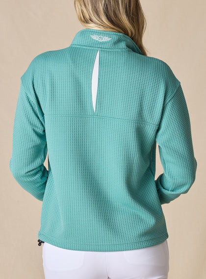 Women's Opal Half Zip in Sea Green, back view on model featuring a sea green waffle-textured pullover with an embroidered Straight Down logo at the collar and a white center back vent detail paired with white pants