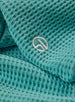 Women's Opal Half Zip in Sea Green, close-up detail view featuring the waffle-texture fabric and embroidered Straight Down logo at the hem