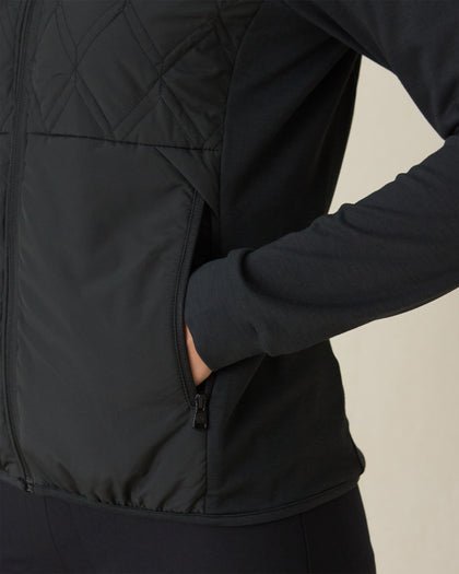 Women's Hera Jacket in Black, close-up detail view featuring the zippered side pocket with model's hand inserted, showcasing the contrast between the quilted front body and solid knit sleeve