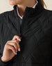 Women's Hera Jacket in Black, close-up detail view featuring the diamond quilted front body and full-zip stand collar, layered over a white polo