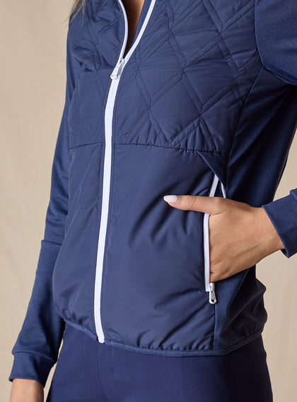 Women's Hera Jacket in New Indigo, close-up detail view featuring the diamond quilted front body with white contrast zipper and model's hand in the white zippered side pocket, showcasing the navy performance fabric