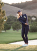 Women's Althea Half Zip in New Indigo, on-course action view featuring a model completing a golf swing wearing the navy half zip with matching navy pants and white shoes on a golf course