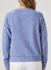 Delia Sweatshirt in Blueberry, back view on model featuring a medium blue ribbed-texture crewneck pullover with raglan sleeves and white embroidered logo detail at the center back neck styled with white pants