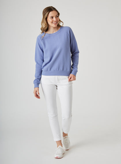 Delia Sweatshirt in Blueberry, full length front view on model featuring a medium blue ribbed-texture crewneck pullover with raglan sleeves and ribbed hem styled with white pants and white shoes