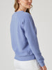 Delia Sweatshirt in Blueberry, back angle view on model featuring a medium blue ribbed-texture crewneck pullover with raglan sleeves and tonal embroidered logo detail at the upper back styled with white pants