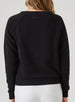 Delia Sweatshirt in Black, back view on model featuring a black ribbed-texture crewneck pullover with raglan sleeves and tonal embroidered logo detail at the center back neck styled with white pants