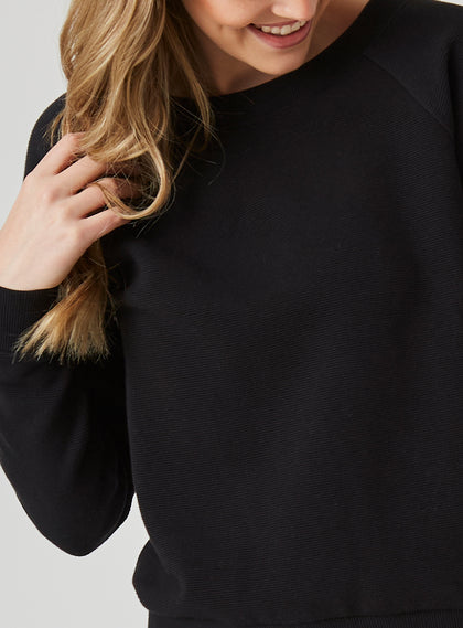 Delia Sweatshirt in Black, close-up front view on model featuring the ribbed-texture fabric and raglan sleeve seam detail at the crewneck collar