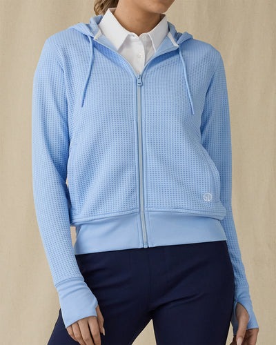 Eliza Hoodie in Carolina, front view on model showing a light blue waffle-knit full zip hoodie with drawstring hood, layered over a white polo, paired with navy pants