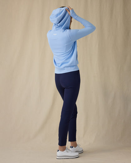Eliza Hoodie in Carolina, full length back view on model showing a light blue waffle-knit full zip hoodie with hood up, paired with navy pants and white golf shoes