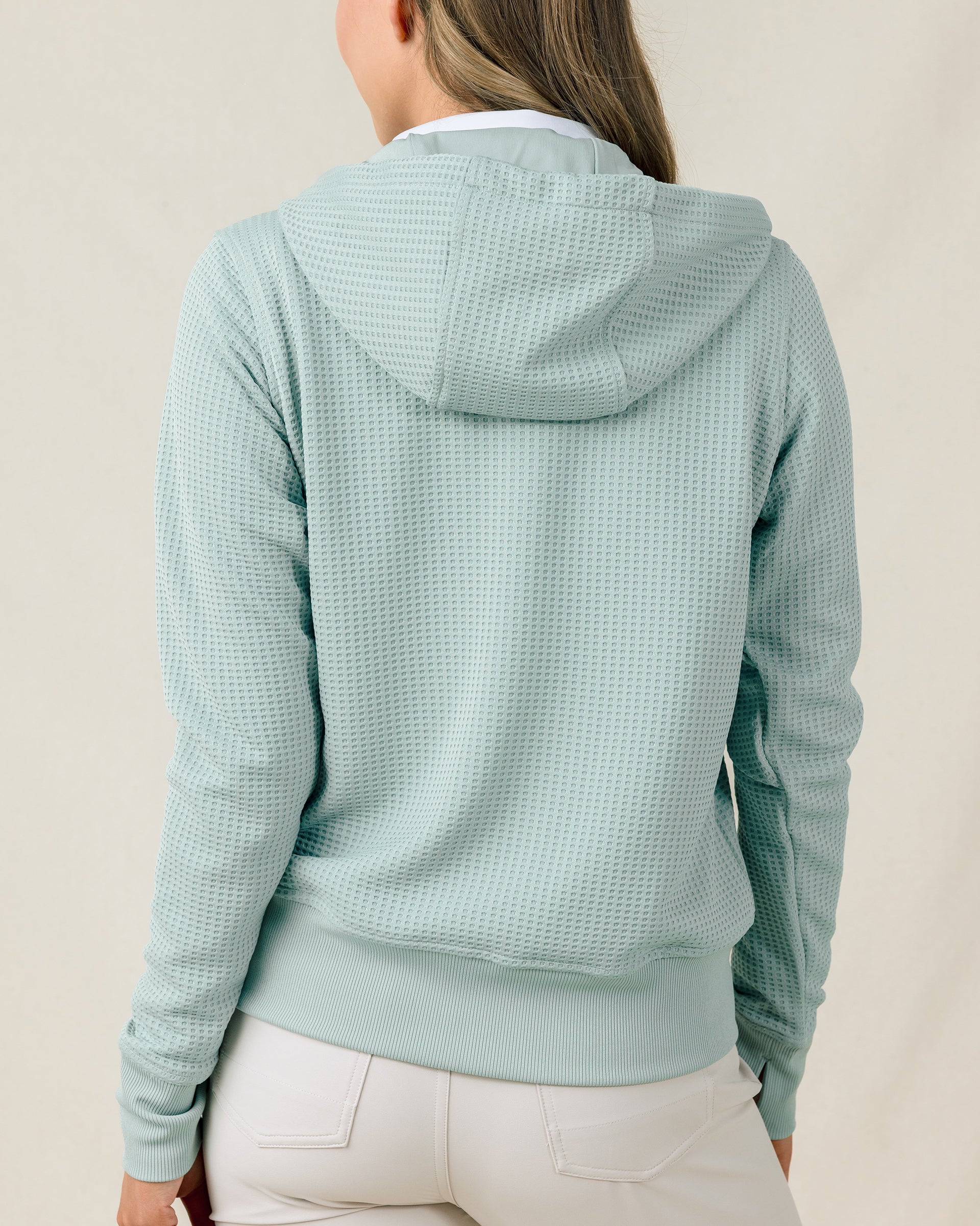 Back view of a model wearing the Eliza Hoodie in Herb, showing the hood and textured waffle knit.