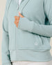 Close-up of the Eliza Hoodie in Herb highlighting the waffle knit texture, thumbhole cuff, front pocket, ribbed hem, and embroidered logo.