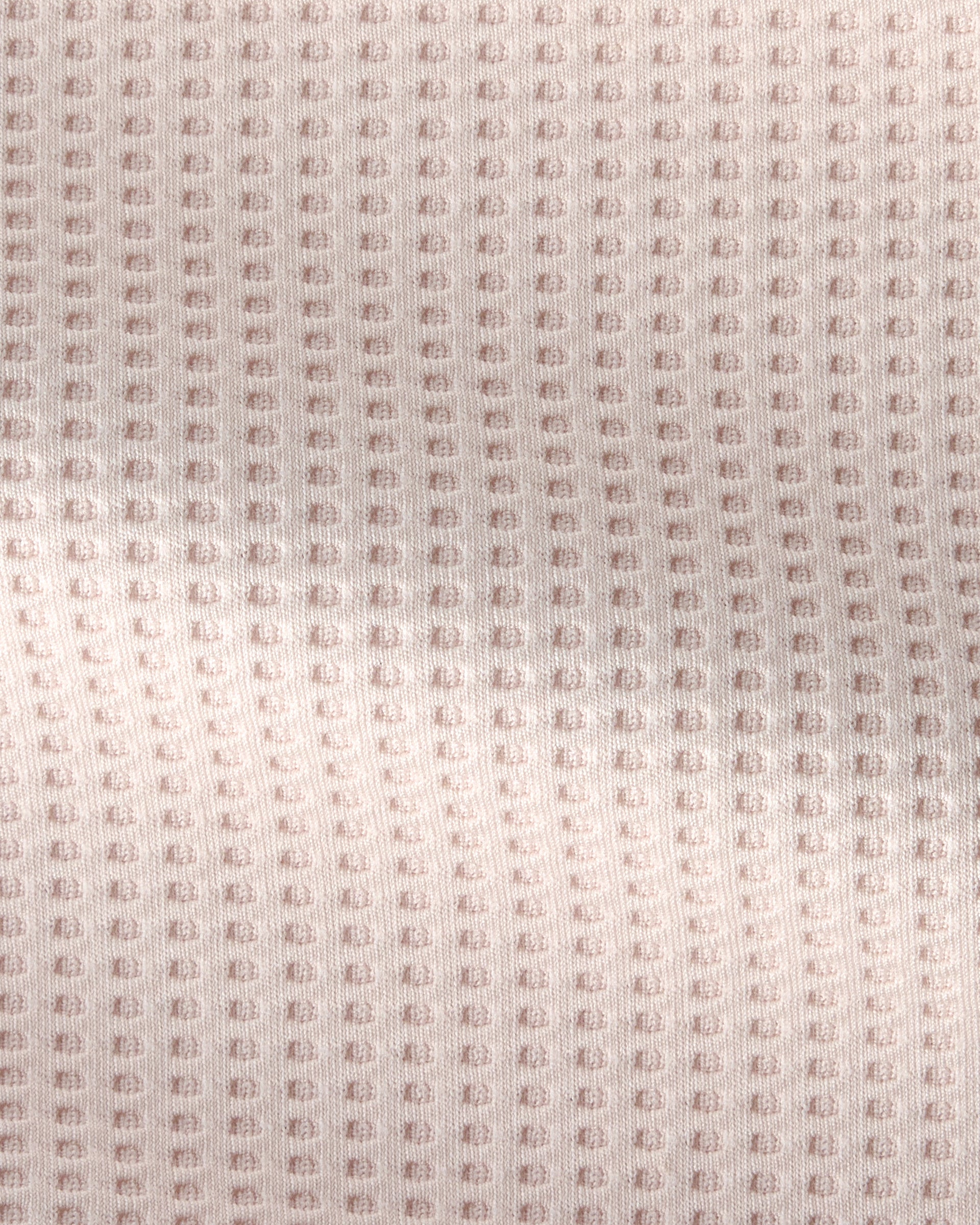 A close-up of a textured fabric with a repeating waffle or bubble pattern in a very light blush pink color.