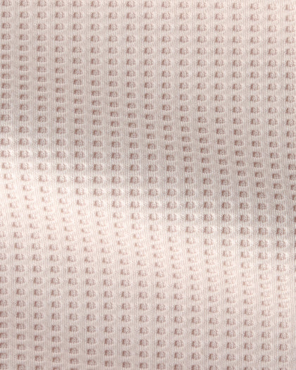 A close-up of a textured fabric with a repeating waffle or bubble pattern in a very light blush pink color.