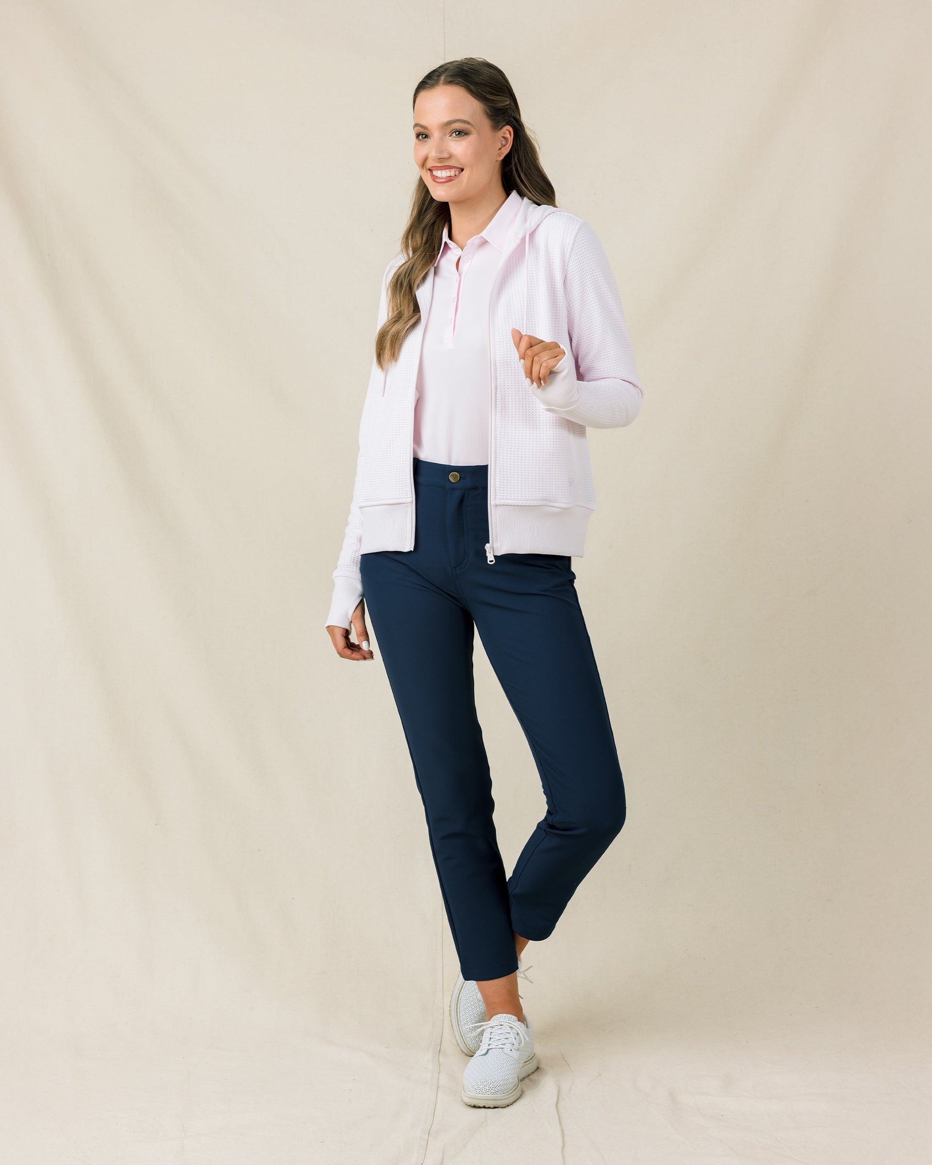 Woman wearing the Straight Down Eliza Hoodie in Pale Pink unzipped over a pale pink polo with navy golf pants