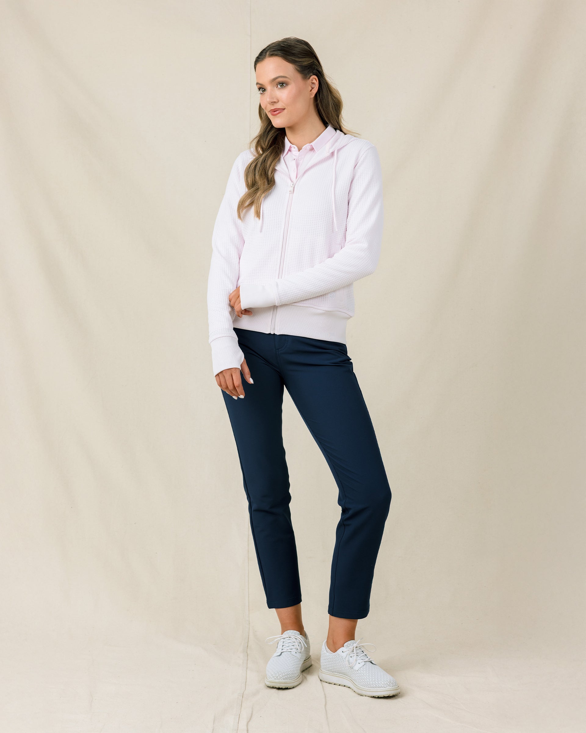 Woman wearing the Straight Down Eliza Hoodie in Pale Pink zipped up with navy golf pants