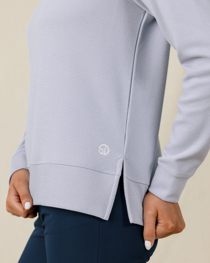 Close-up of the Daria Hoodie in Cosmic Blue showing the waffle-knit texture, side slit hem, and embroidered logo