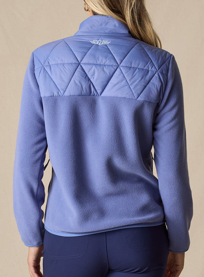 Women's Laurel Hybrid Fleece Jacket in Blueberry, back view on model featuring a medium blue quilted diamond-pattern upper back panel with fleece lower body and an embroidered Straight Down logo at the collar paired with navy pants