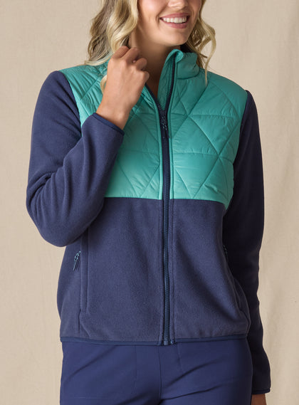 Women's Laurel Hybrid Fleece Jacket in Sea Green and New Indigo, front view on model featuring a sea green quilted upper body with navy fleece lower body and sleeves, full-zip closure, and side zip pocket paired with navy pants