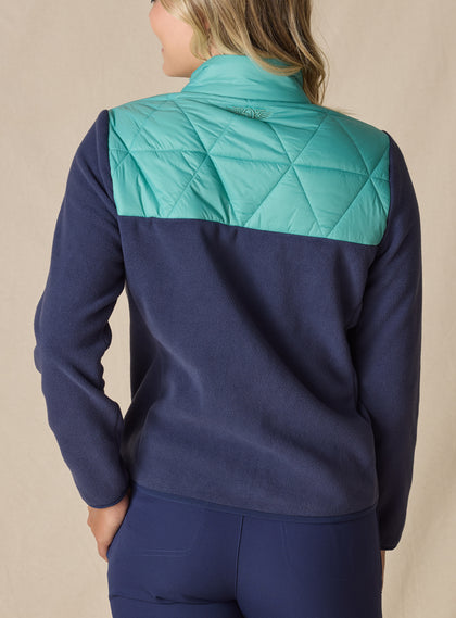 Women's Laurel Hybrid Fleece Jacket in Sea Green and New Indigo, back view on model featuring a sea green quilted upper back panel with navy fleece lower body and an embroidered Straight Down logo at the collar paired with navy pants