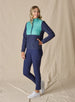 Women's Laurel Hybrid Fleece Jacket in Sea Green and New Indigo, front full body view on model featuring a sea green quilted upper body with navy fleece lower body and sleeves paired with navy pants and white golf shoes