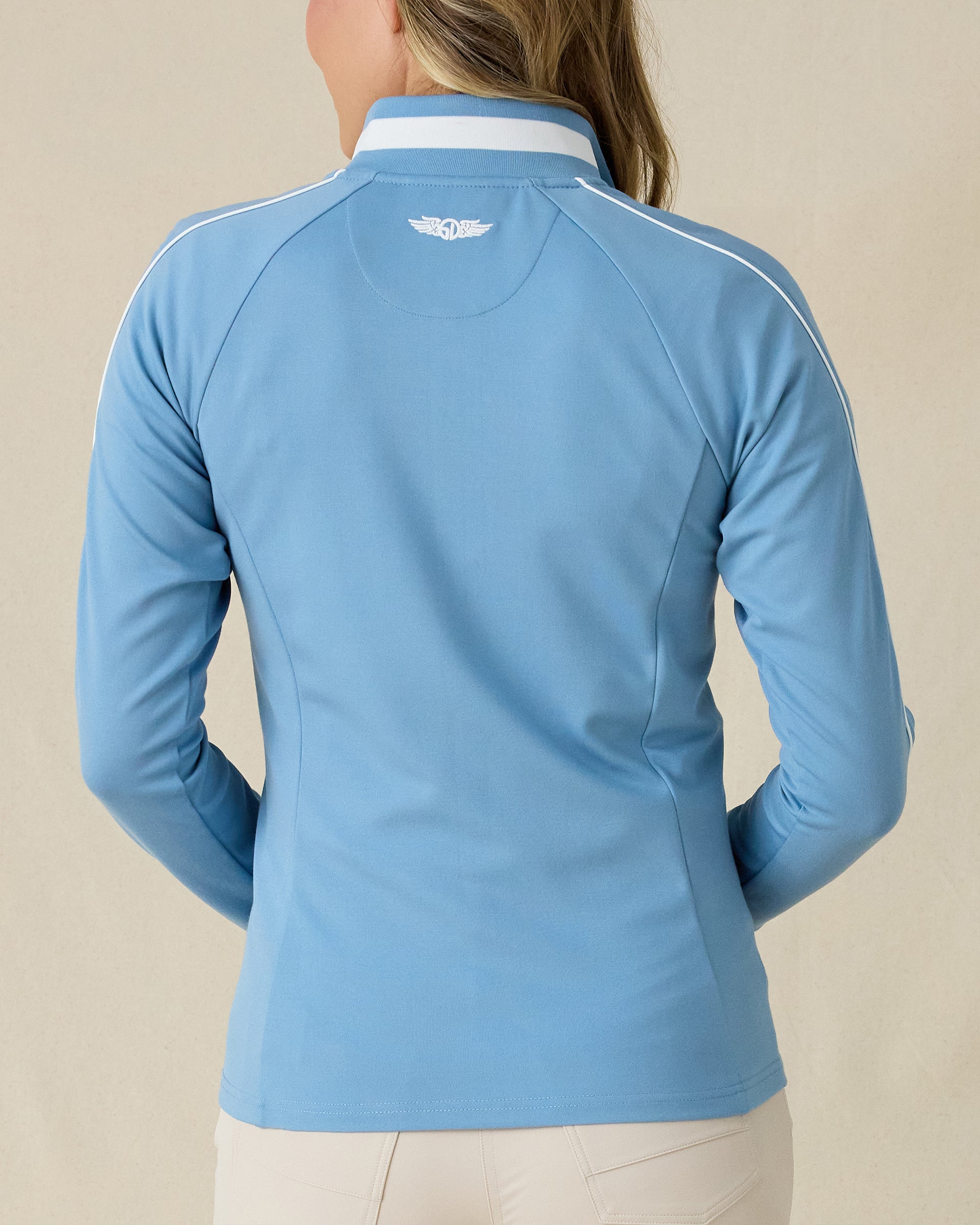 Patty Jacket in Coastal, back view on model featuring a solid medium blue full zip jacket with white piping along the sleeves and Straight Down embroidered logo at the upper back, paired with khaki pants