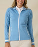 Patty Jacket in Coastal, front view on model featuring a solid medium blue full zip jacket with white piping along the sleeves and white striped cuffs, layered over a white polo and paired with khaki pants