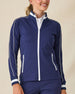 Patty Jacket in New Indigo, front view on model in solid navy with white contrast piping and full zip, layered over a white polo