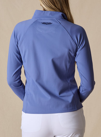 Women's Eirene Jacket in Blueberry, back view on model featuring a solid cornflower blue performance fabric with raglan sleeve construction and tonal Straight Down logo at the upper back, paired with white pants