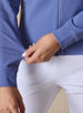 Women's Eirene Jacket in Blueberry, close-up detail view featuring the zippered side pocket with model's hand at the hem, showcasing the solid cornflower blue performance fabric and ribbed cuff, paired with white pants