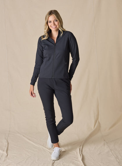 Women's Eirene Jacket in Black, full-length front view on model featuring a solid black performance fabric with a full-zip stand collar and raglan sleeves, paired with matching black pants and white shoes