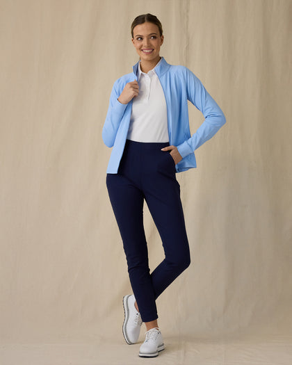 Women's Eirene Jacket in Carolina, full length front view on model featuring a light blue full-zip jacket with mock neck collar worn open over a white polo, paired with navy pants and white golf shoes