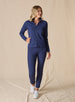 Women's Eirene Jacket in New Indigo, full-length front view on model featuring a solid navy performance fabric with a full-zip stand collar and raglan sleeves, with hand in zippered side pocket, paired with matching navy pants and white shoes