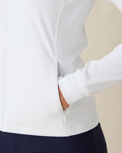 Women's Eirene Jacket in White, close-up detail view featuring a zippered side pocket with model's hand inserted, showcasing the clean white performance fabric and ribbed cuff
