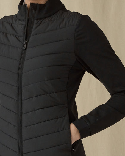Women's Ida Hybrid Jacket in Black, close-up detail view featuring the quilted front body panel, smooth stretch sleeve, and full zip on a black hybrid jacket