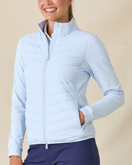 Women's Ida Hybrid Jacket in Lake, front view on model featuring a light blue hybrid jacket with quilted puffer front body and stretch knit sleeves, layered over a white polo, paired with navy pants