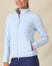 Women's Ida Hybrid Jacket in Lake, front view on model featuring a light blue hybrid jacket with quilted puffer front body and stretch knit sleeves, layered over a white polo, paired with navy pants