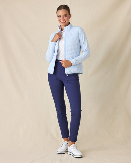 Women's Ida Hybrid Jacket in Lake, full length front view on model featuring a light blue hybrid jacket with quilted puffer front body worn open, layered over a white polo, paired with navy pants and white golf shoes